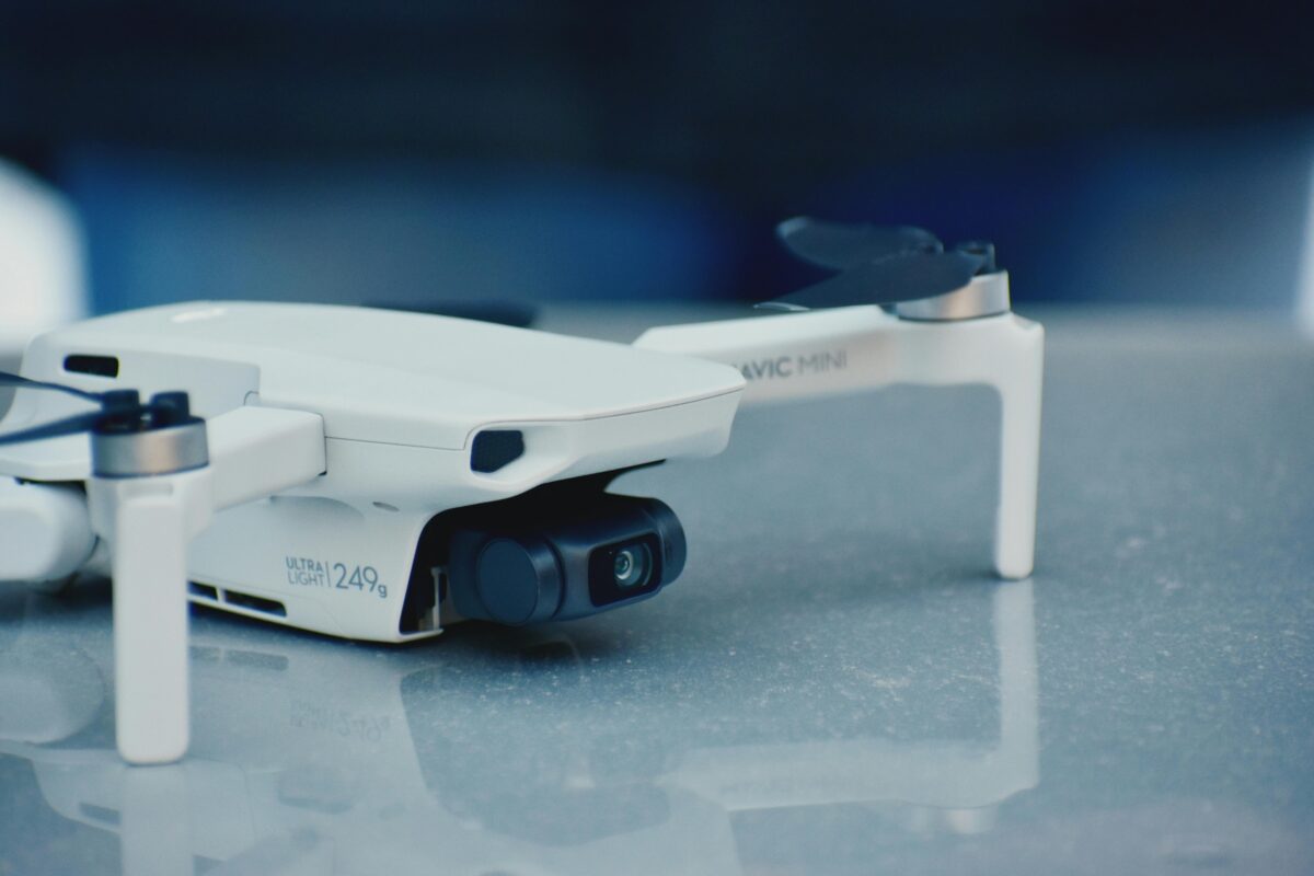 Close-up of a white drone on a reflective surface, showcasing its camera and sleek design.